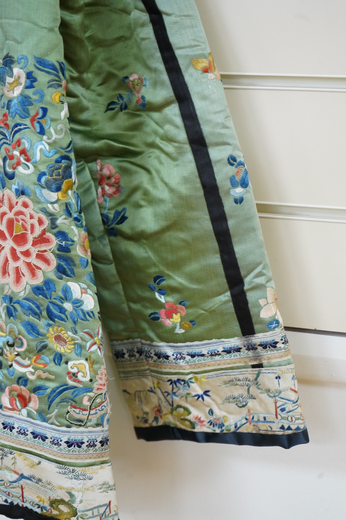 An early 20th century Chinese green silk polychrome embroidered jacket. Worked with Chinese knot embroidery and stem stitch into flowers, butterflies and bats, edged with woven silk ribbon and a figurative embroidered bo
